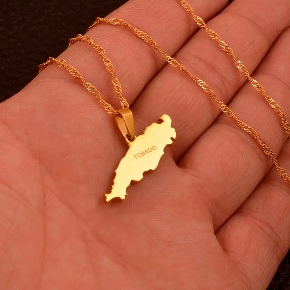 A gold necklace with a map-shaped pendant engraved with the word 'TOBAGO', displayed on a person's hand.